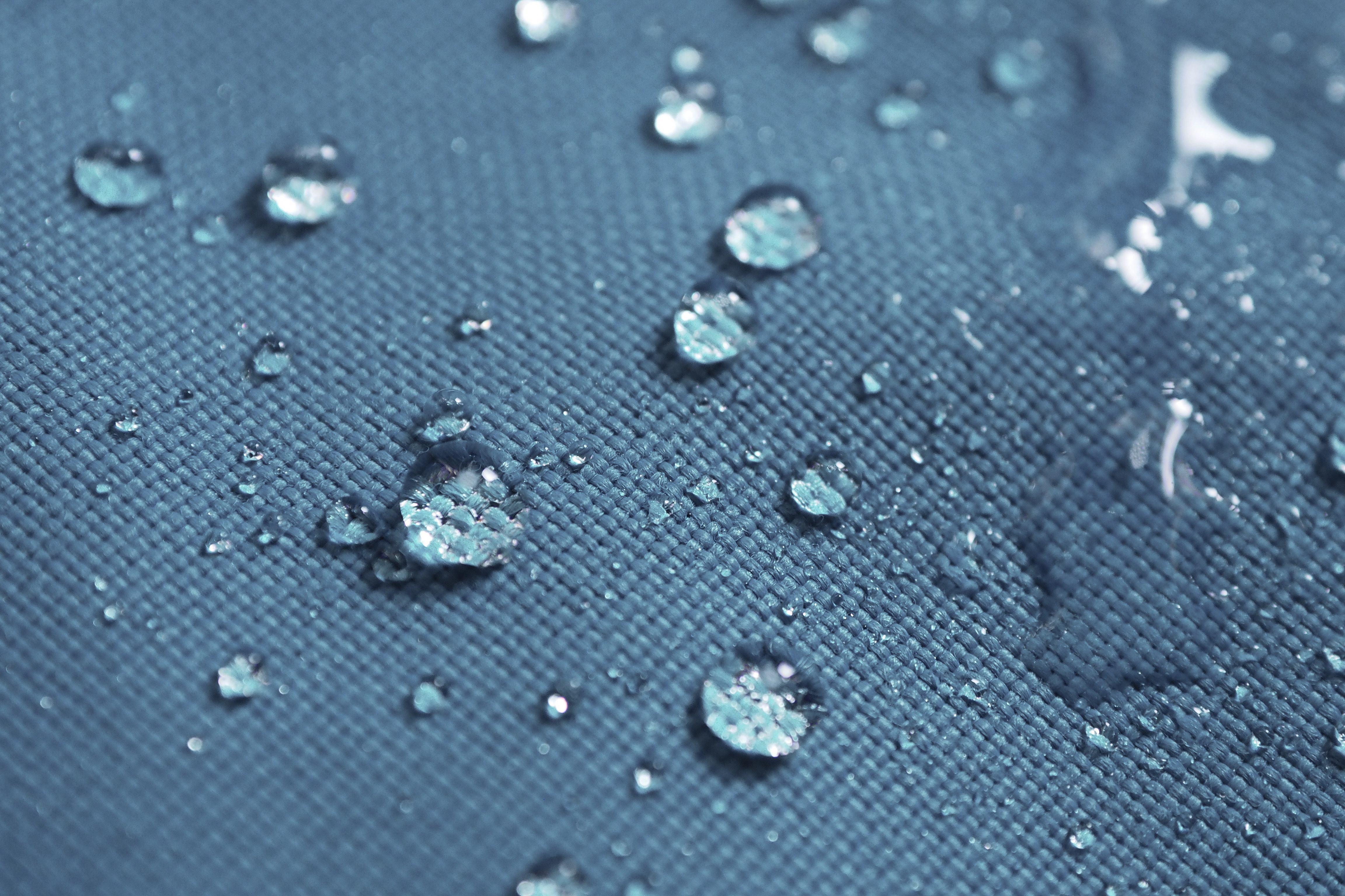 Closeup of water drops on dark blue and grey fabric with waterproof design to protect fabric.