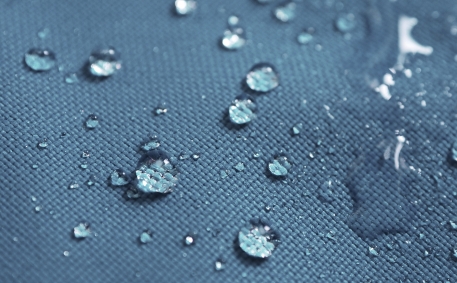 Closeup of water drops on dark blue and grey fabric with waterproof design to protect fabric.